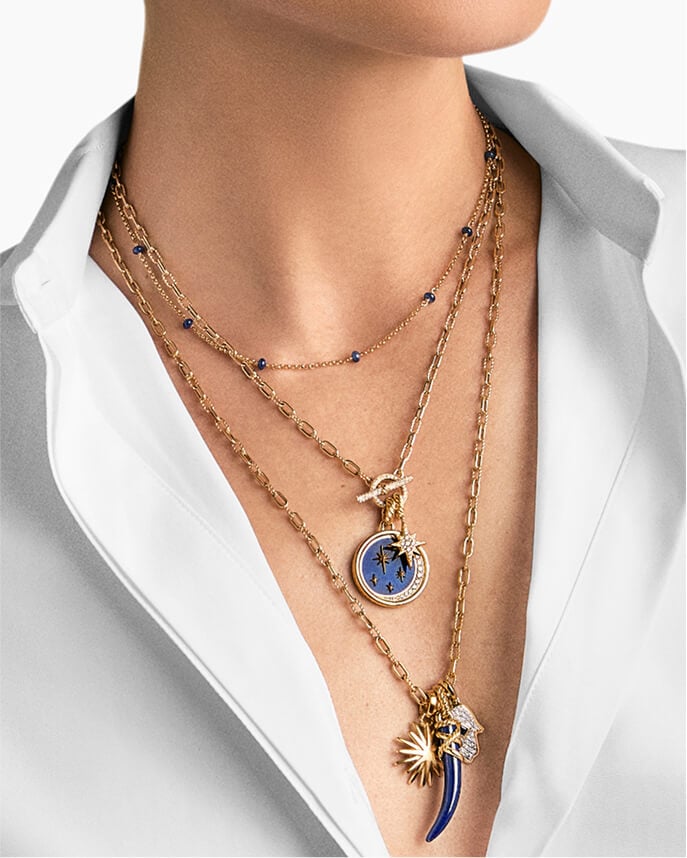 A woman layering three David Yurman necklaces with amulets.